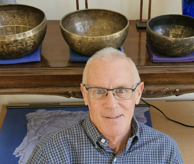 Man with glasses in front of table with three singing bowls.